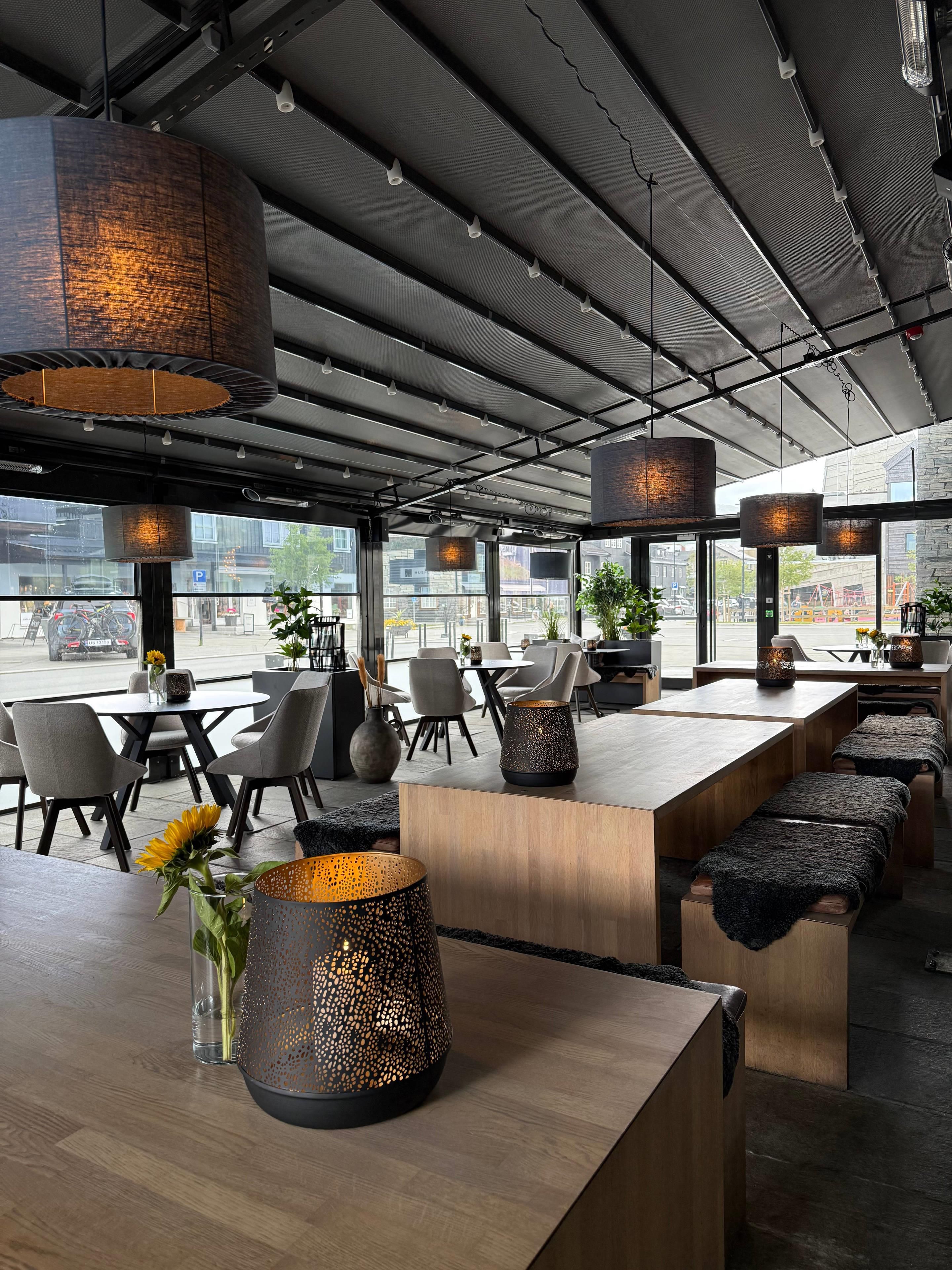 A modern restaurant interior with high ceilings, pendant lighting, and a view of the cityscape.
