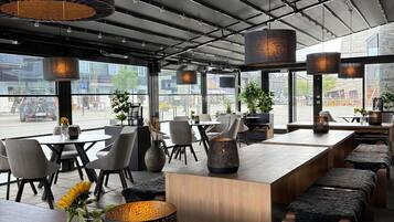 A modern restaurant interior with high ceilings, pendant lighting, and a view of the cityscape.