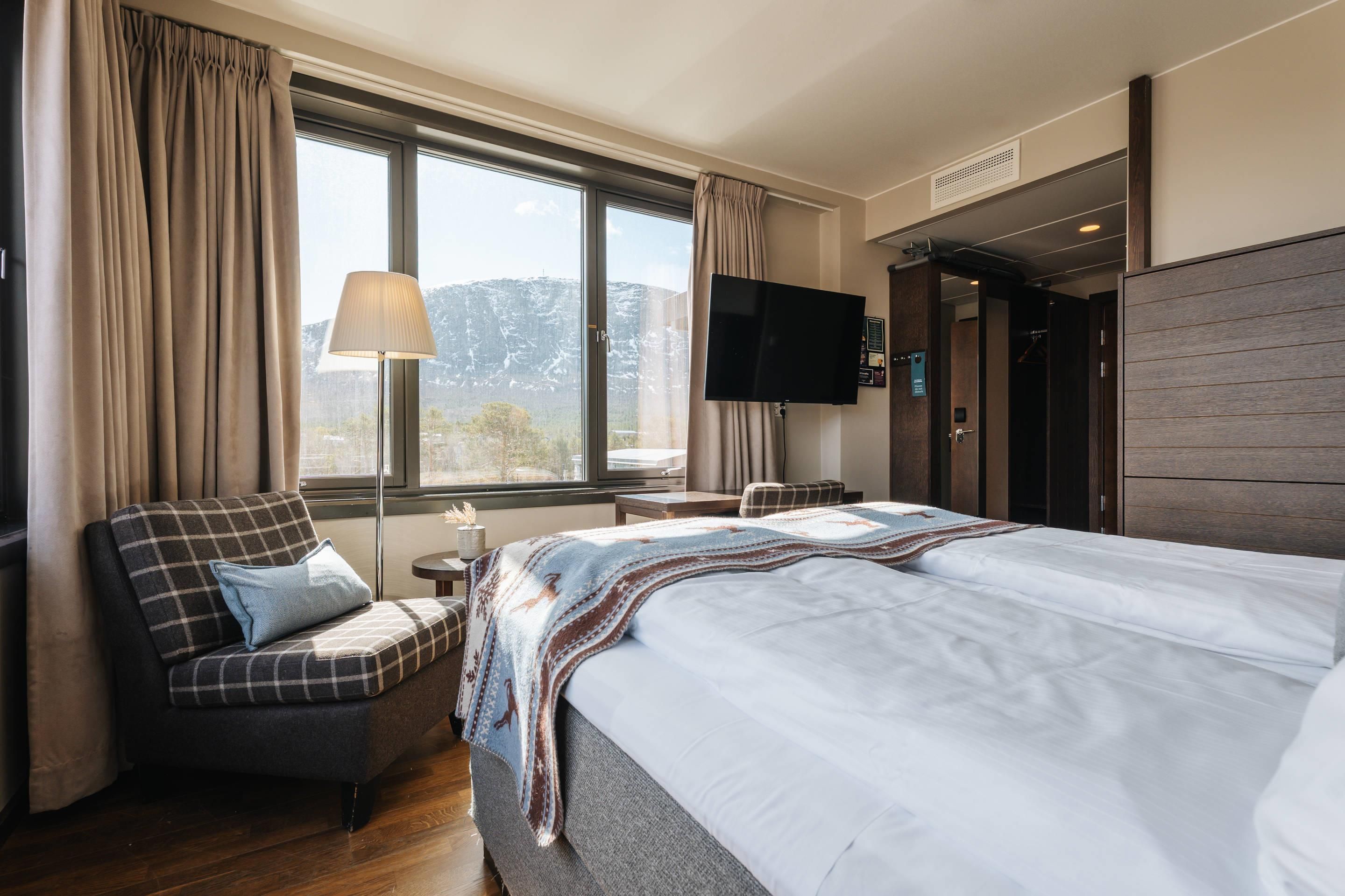A hotel room with a bed, a chair, a TV, and a window with curtains.
