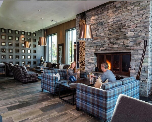 A modern living room with a stone fireplace, sofas, and a large window.