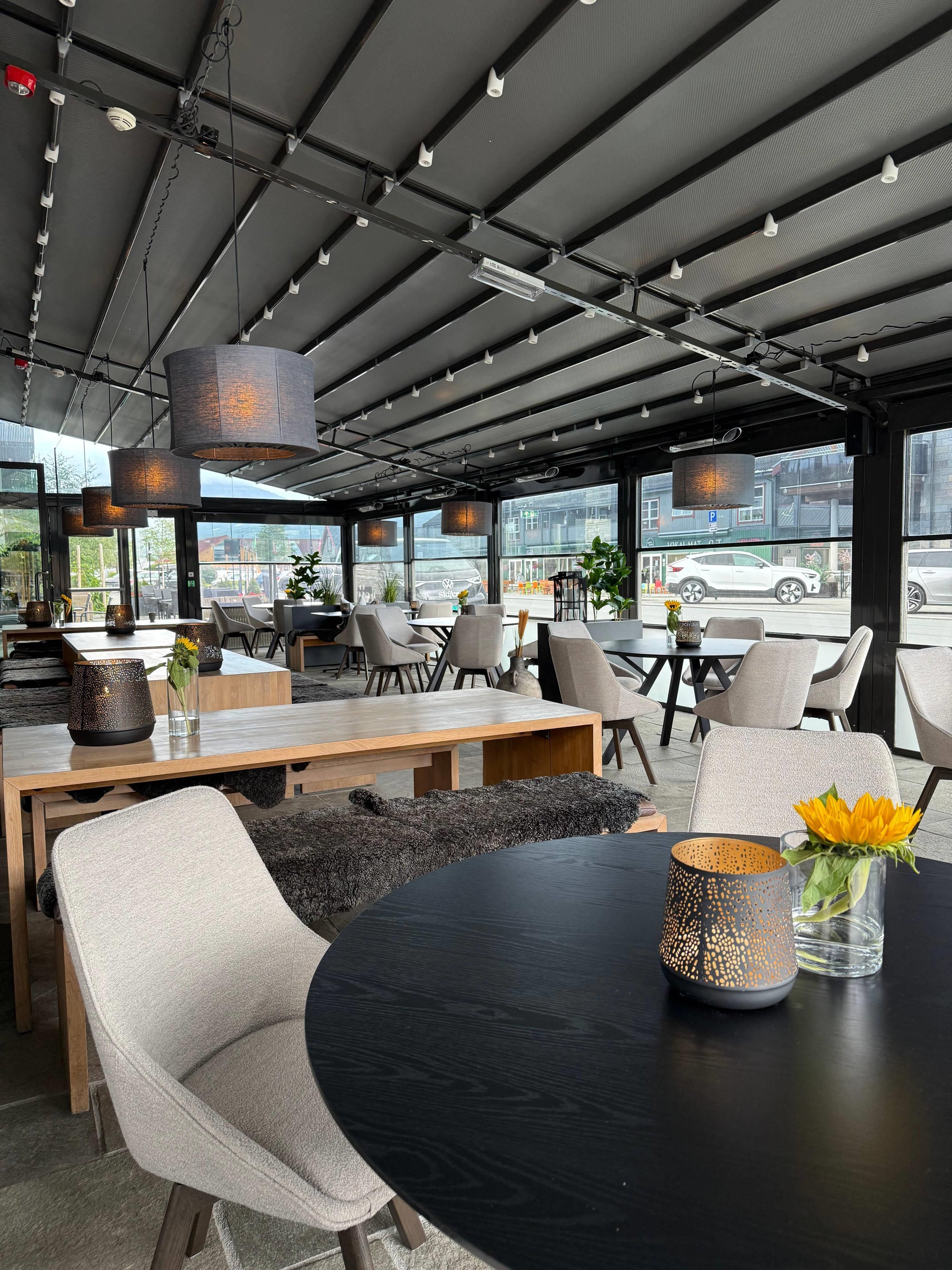 An indoor seating area with tables and chairs, large windows, and hanging pendant lights.