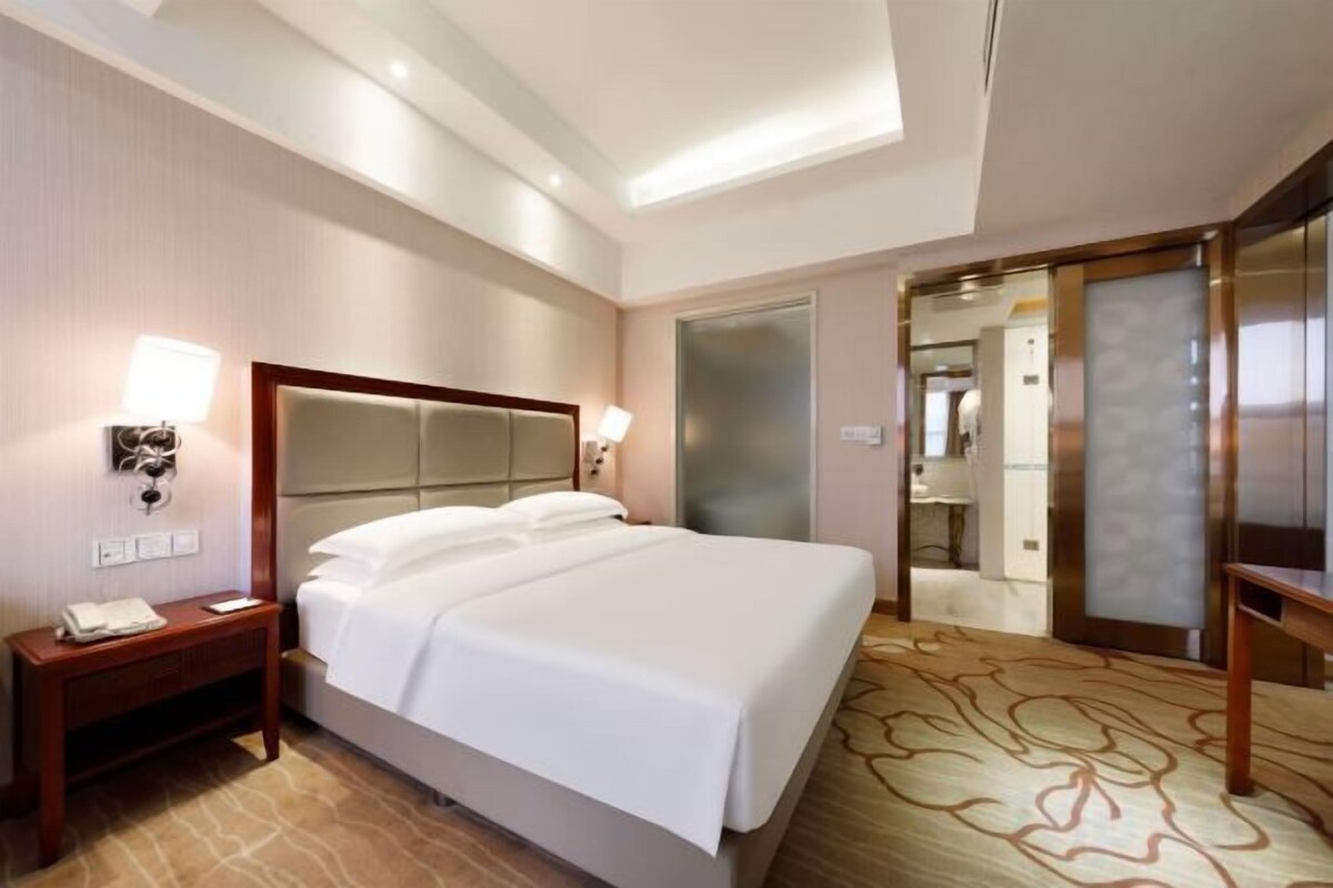 A hotel room with a large bed, bedside tables, a desk, and a mirror.