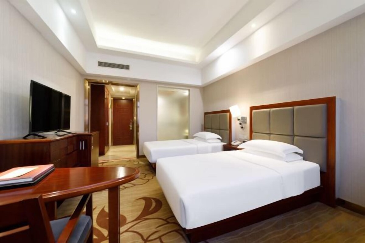 A hotel room with two beds, a desk, a television, and a door leading to a bathroom.