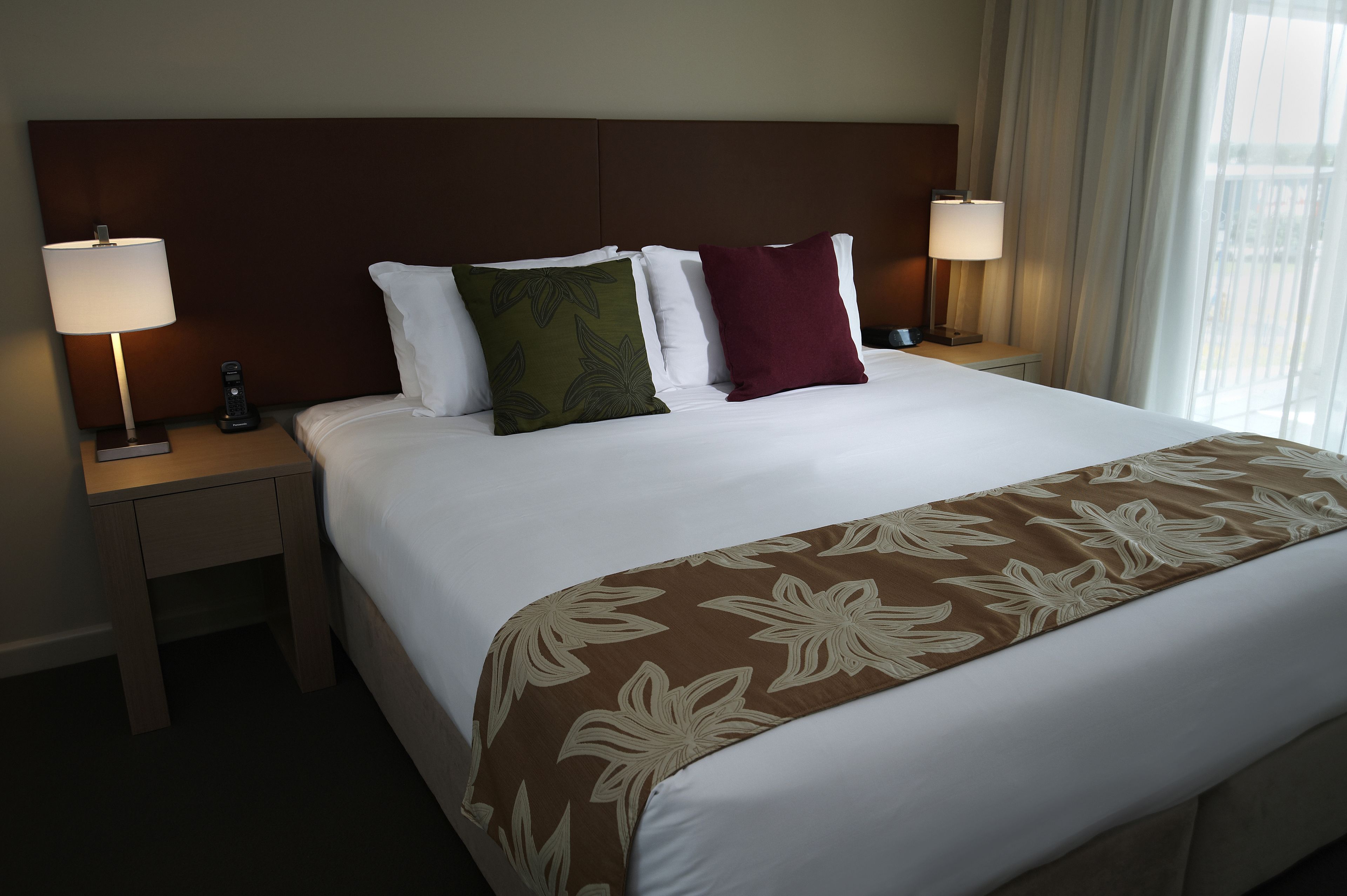 A neatly made bed with a floral-patterned bedspread, two bedside lamps, and a nightstand with a coffee maker.