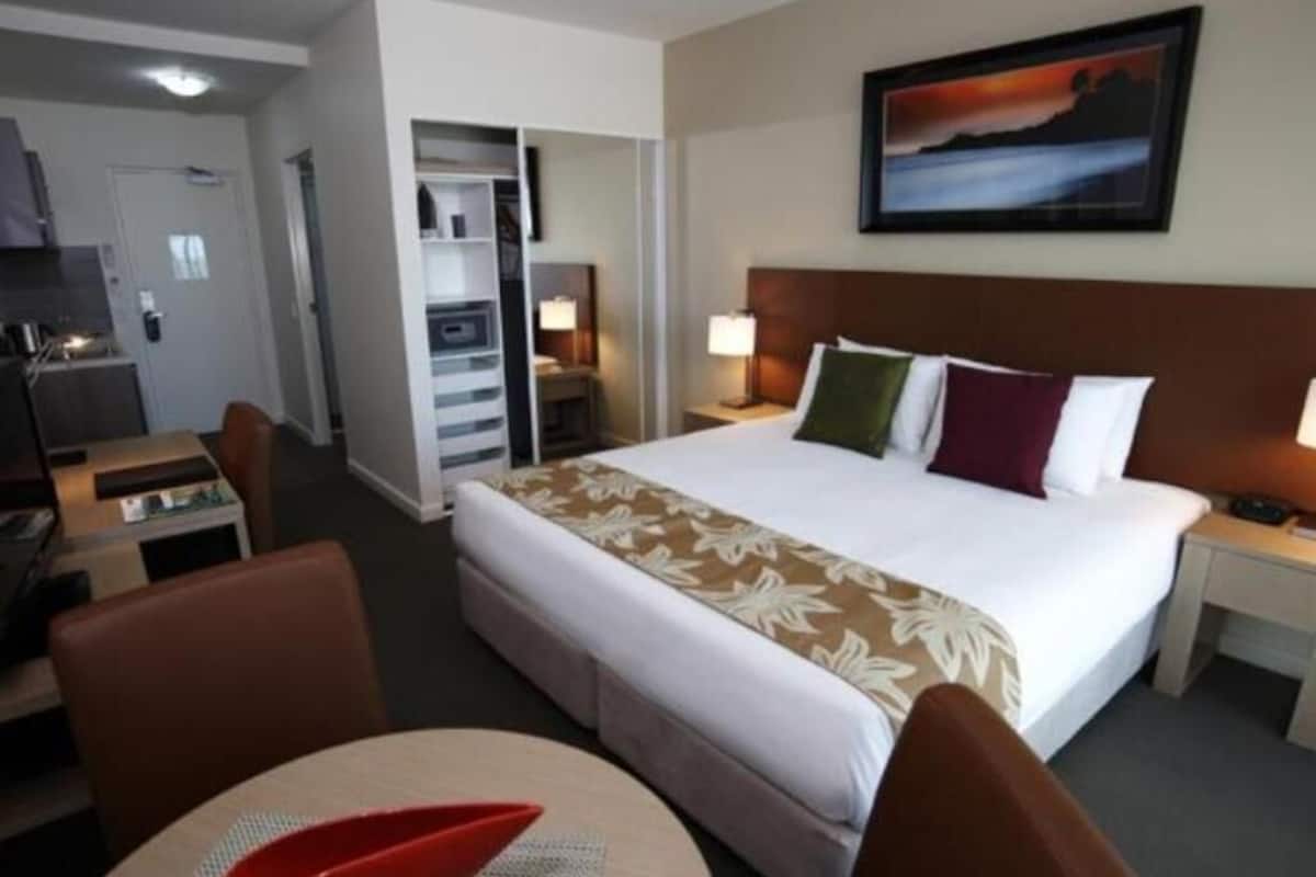 Habitación de hotel con cama, escritorio, silla, mesa de comedor y un cuadro en la pared.