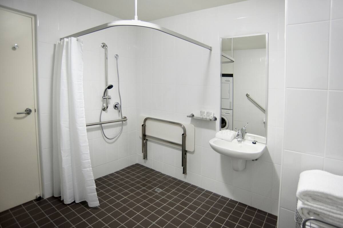 Un baño moderno con ducha, barra de apoyo, lavabo y espejo.