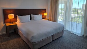 Ett hotellrum med en stor säng, två sängbord med lampor, en sänggavel och en balkong med utsikt.