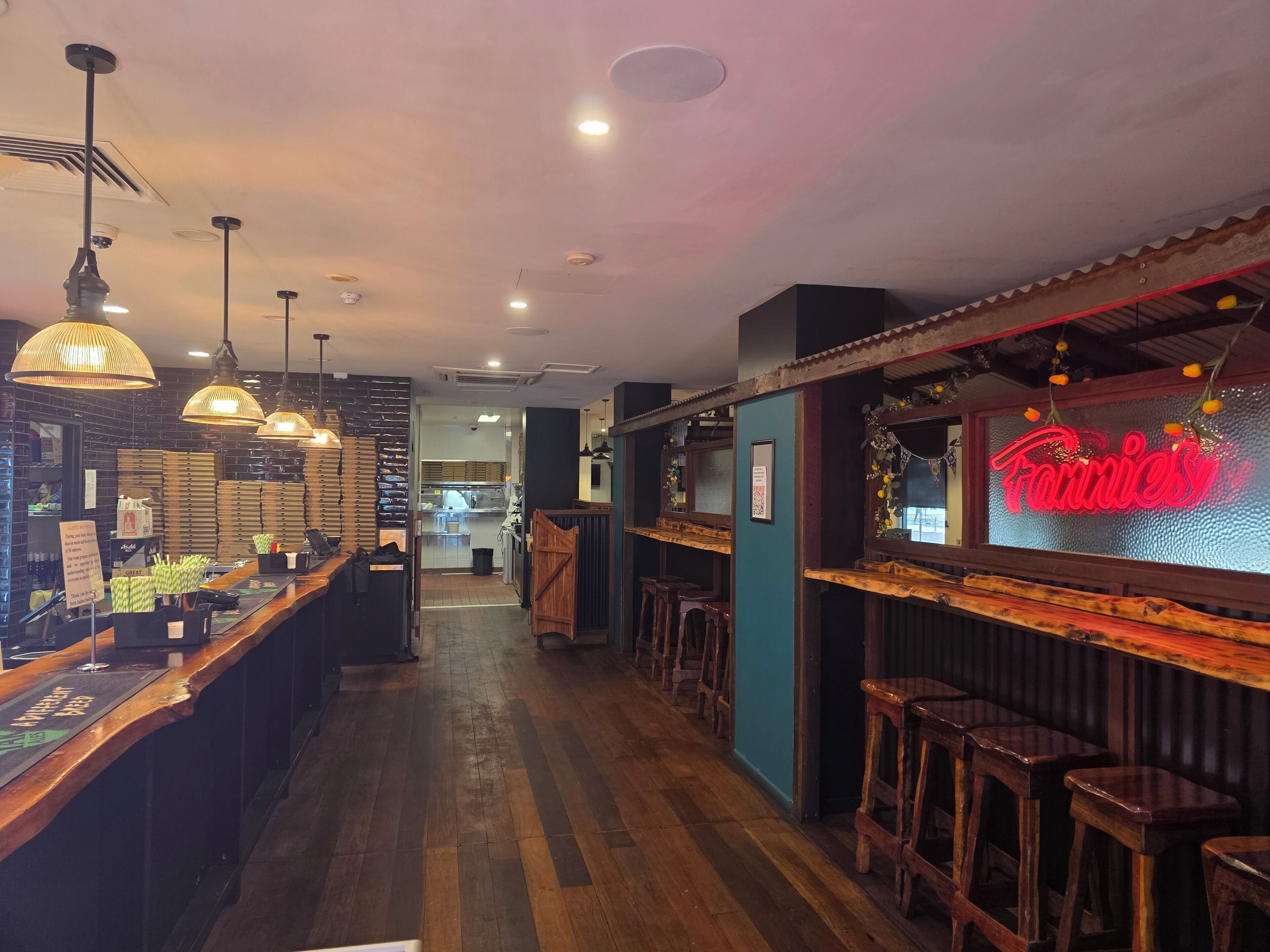A restaurant interior with a bar area, wooden flooring, hanging pendant lights, and a neon sign.