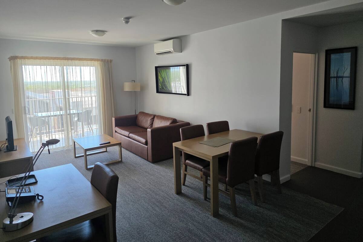 Una sala de estar con sofá, una mesa de comedor con sillas, televisor y lámpara.
