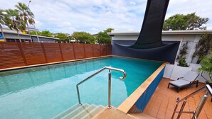En swimmingpool med ett metallräcke, trappsteg som leder ner i poolen och ett kaklat område runt poolen med en stol.