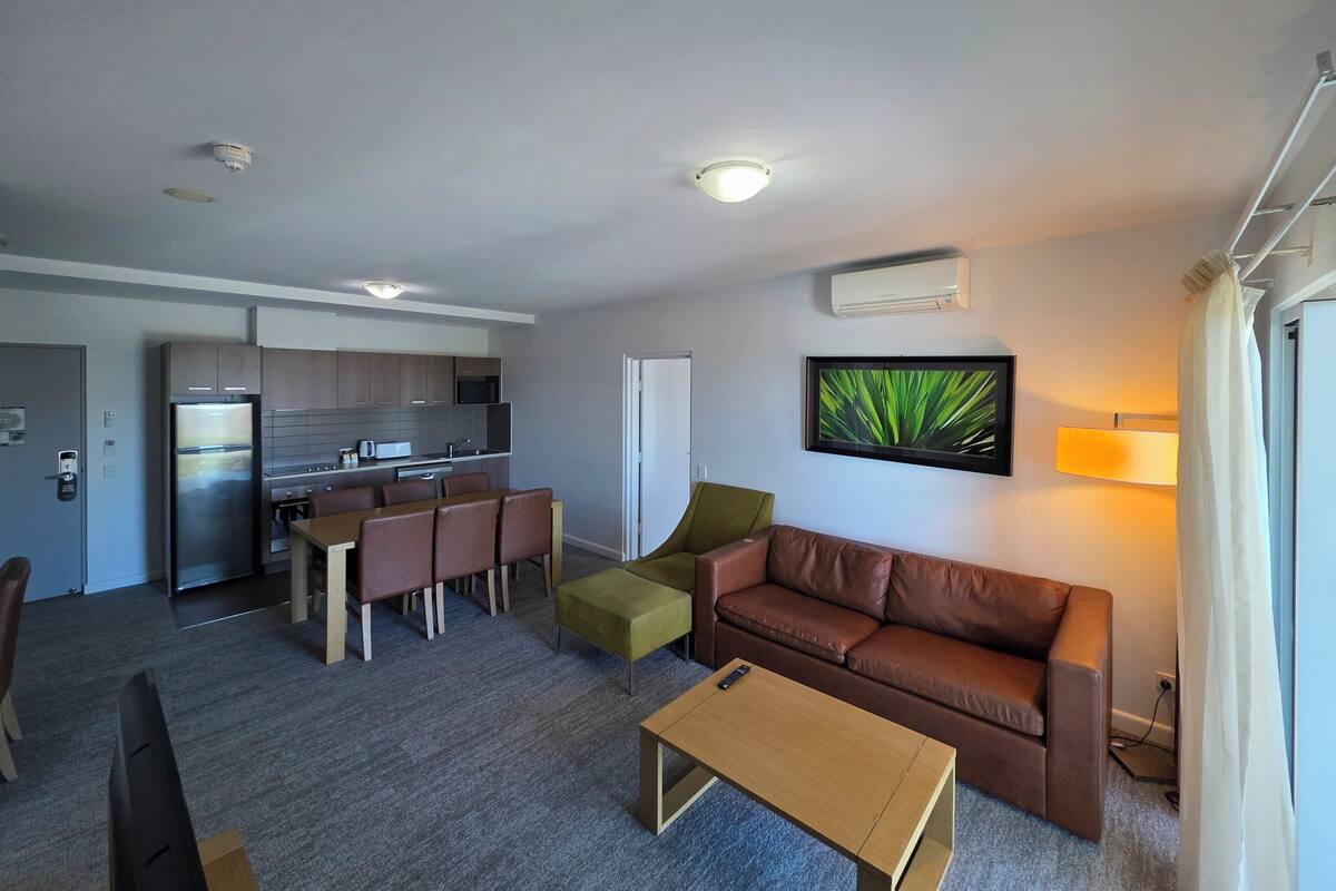 Una sala de estar moderna con un sofá, una mesa de centro y un comedor con sillas, y una cocina al fondo.