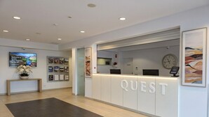 En receptionsdisk märkt med texten ”QUEST”, med en klocka, inramade bilder och en välkomstskylt.