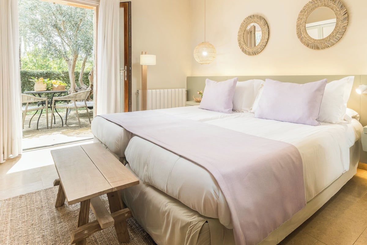 Un dormitorio con una cama grande, mesitas de noche, un banco y vistas al exterior.