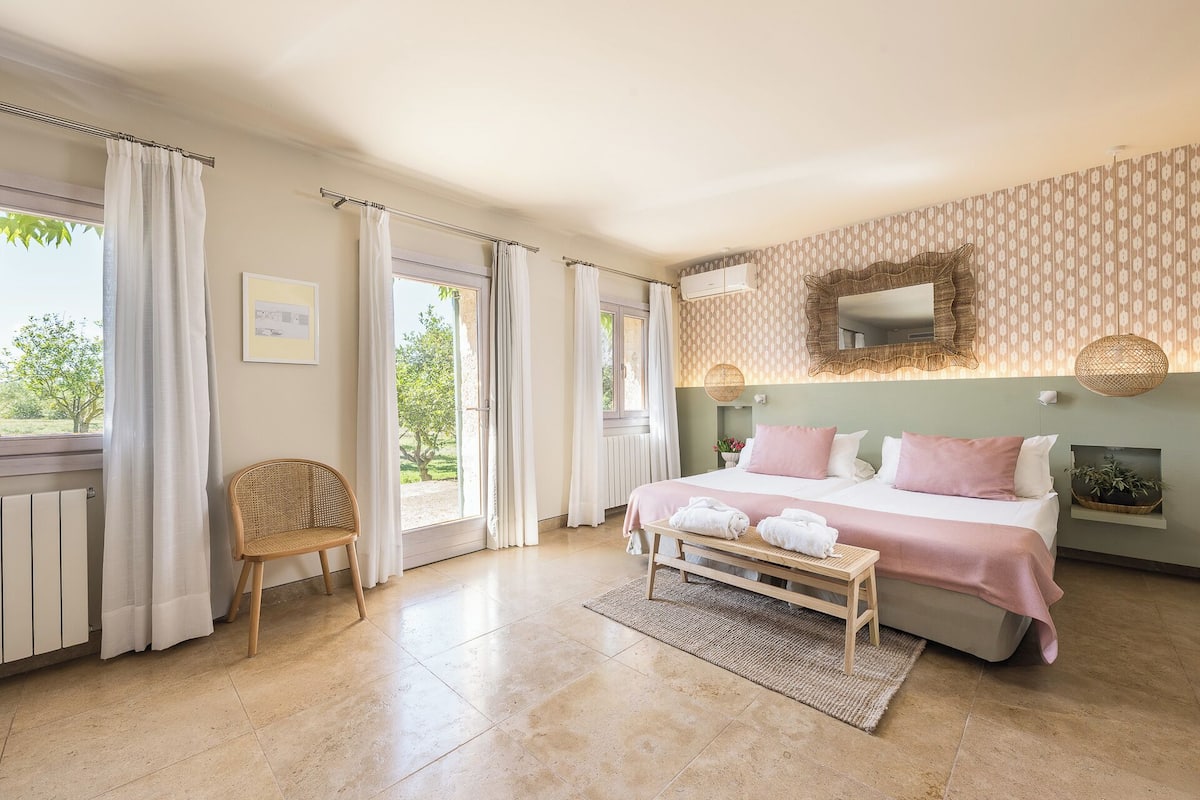 Un dormitorio con cama, una silla, un ventanal y un espejo instalado en la pared.