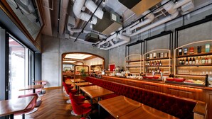 A modern bar area with wooden tables and red chairs, a bar counter with bottles, and a large window providing natural light. - Fraser Residence Nankai Osaka (Osaka)