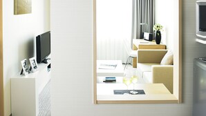 A modern hotel room with a large mirror, a flat-screen TV, a desk with a computer, a sofa, and a dining table with two glasses of wine. - Fraser Residence Nankai Osaka (Osaka)