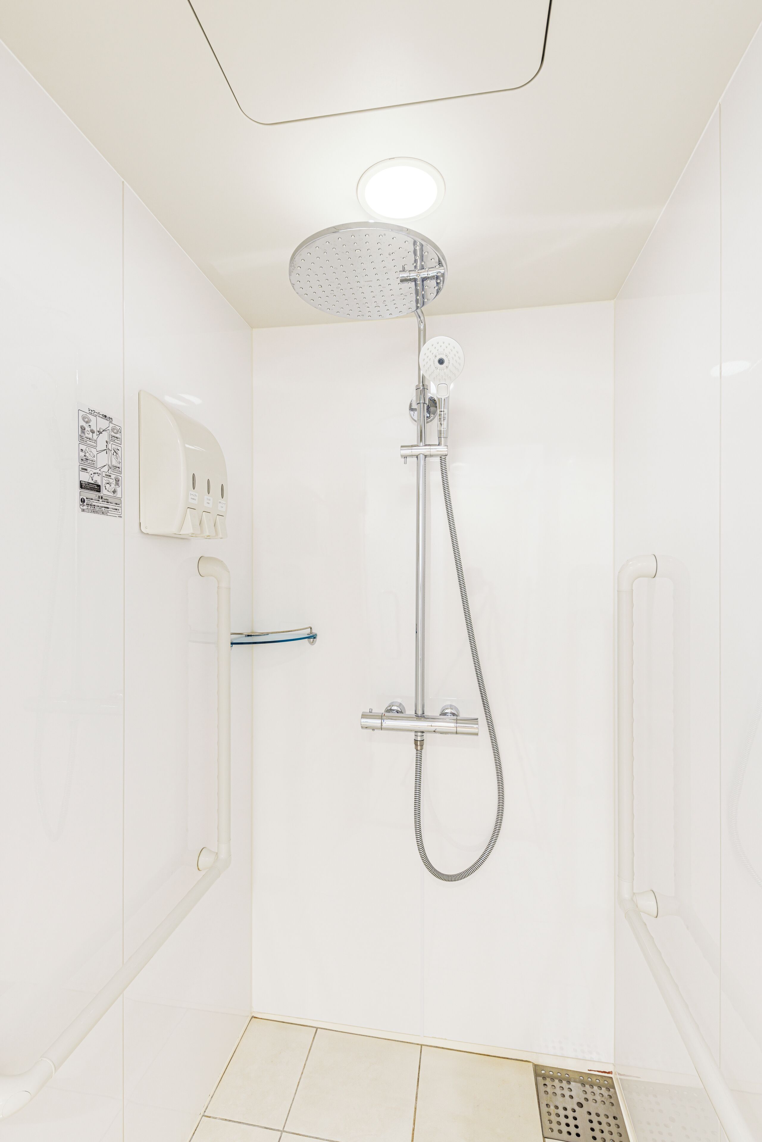 Un baño pequeño y blanco con ducha, un perchero para toallas y un dispensador de jabón de pared.