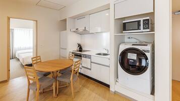 Habitación de hotel compacta con una mesa de comedor de madera, sillas, lavadora integrada, microondas y una kitchenette con pileta y estufa.
