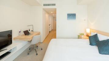 Habitación de hotel con una cama, un escritorio con una computadora portátil, un televisor y una mesita de noche con una lámpara.