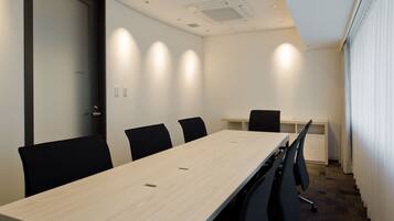 A conference room with a long table, black chairs, a white desk, and a door with frosted glass.