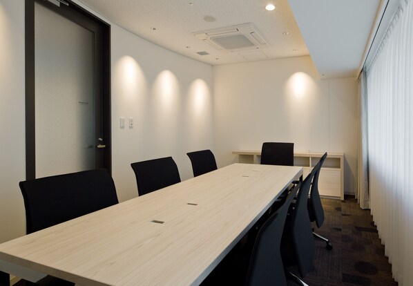Une salle de conférence avec une longue table, des chaises noires, un bureau blanc et une porte en verre dépoli.