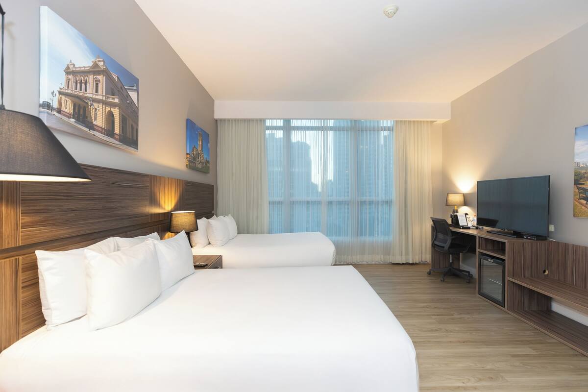 Een hotelkamer met twee bedden, een bureau met televisie en een groot raam met gordijnen.