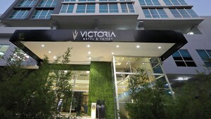 Een moderne hotelentree met een bord waarop 'VICTORIA HOTEL & SUITES' staat.