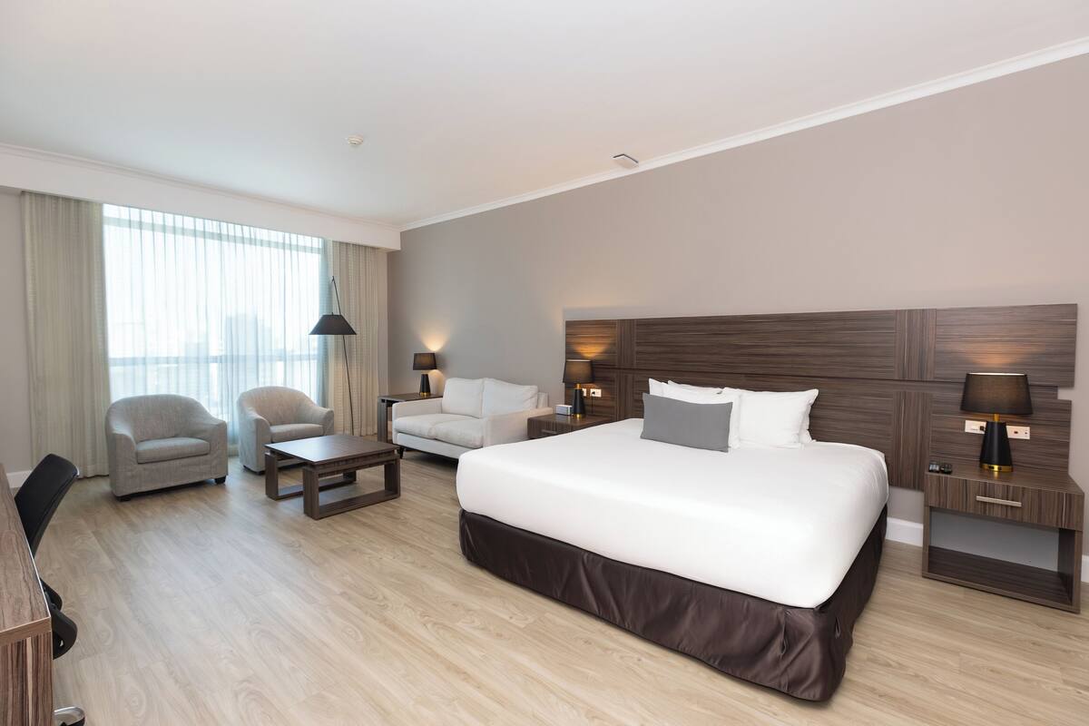 Een moderne hotelkamer met een groot bed, twee fauteuils, een bureau en een lamp.
