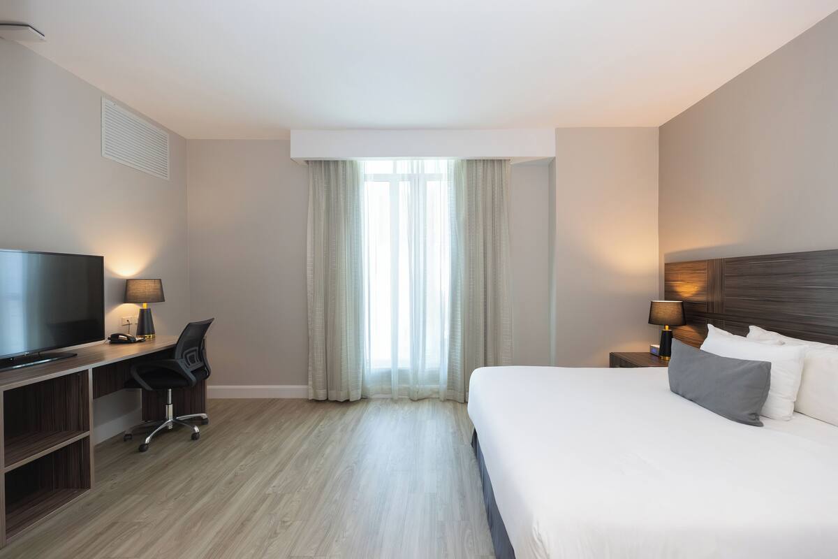Een hotelkamer met een bed, een bureau met stoel, een televisie en twee bedlampen.