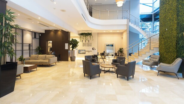 Een ruime lobby met een hoge plafond, een trap en een receptiebalie.