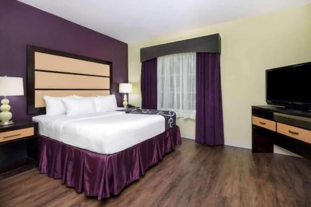 Ein Hotelzimmer mit Bett, Fernseher, Schreibtisch und einem Fenster mit Vorhängen.