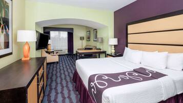 Habitación de hotel con una cama grande, un escritorio con lámpara, televisión y zona de estar con sofá y sillones.