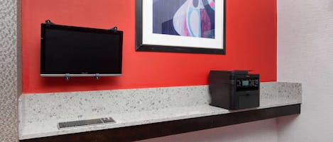 A modern bathroom with a red accent wall, a framed abstract painting, a black towel rack, and a coffee machine on a countertop.