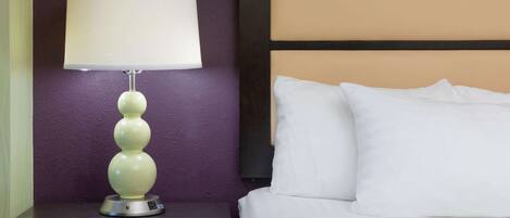A bed with white bedding and a nightstand with a lamp.