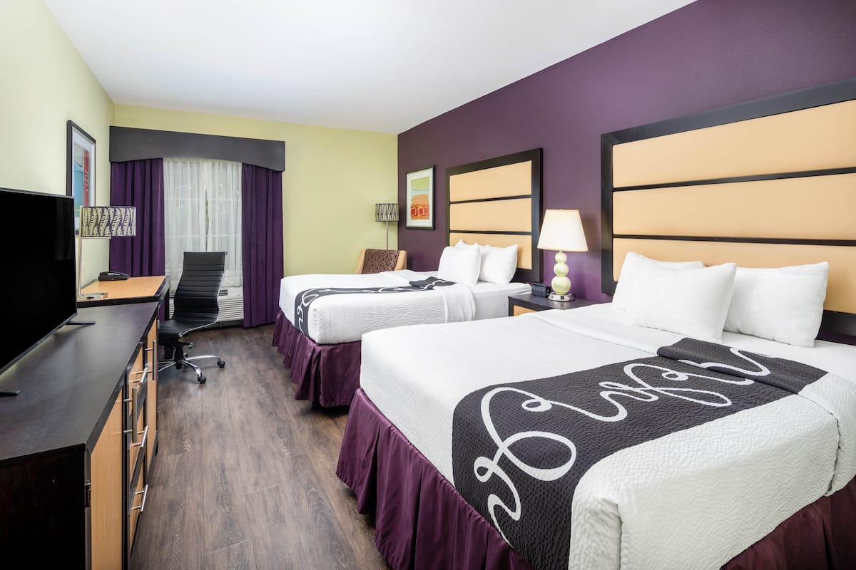 Ein Hotelzimmer mit zwei Betten, einem Schreibtisch, einem Fernseher und einem Sessel.