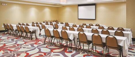 A conference room with rows of tables and chairs, a projector screen, and a patterned carpet.