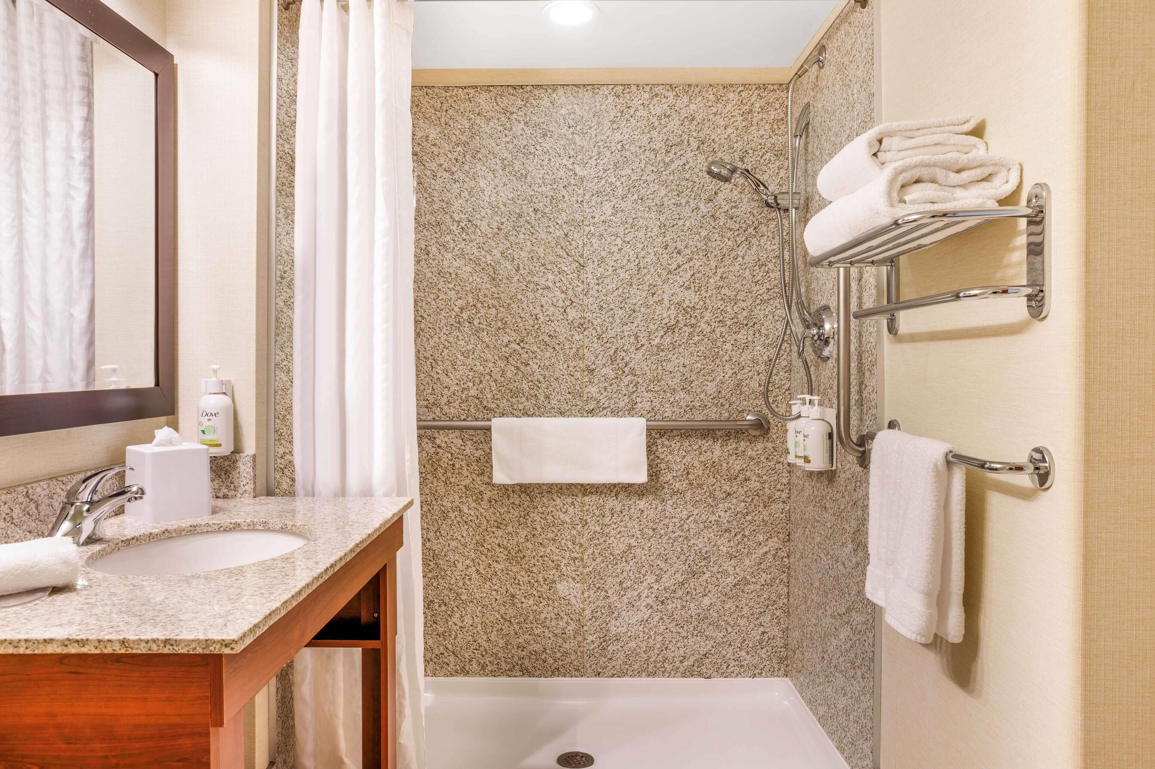 A bathroom with a granite countertop sink, a mirror, a shower with a towel rack, and a bathtub.