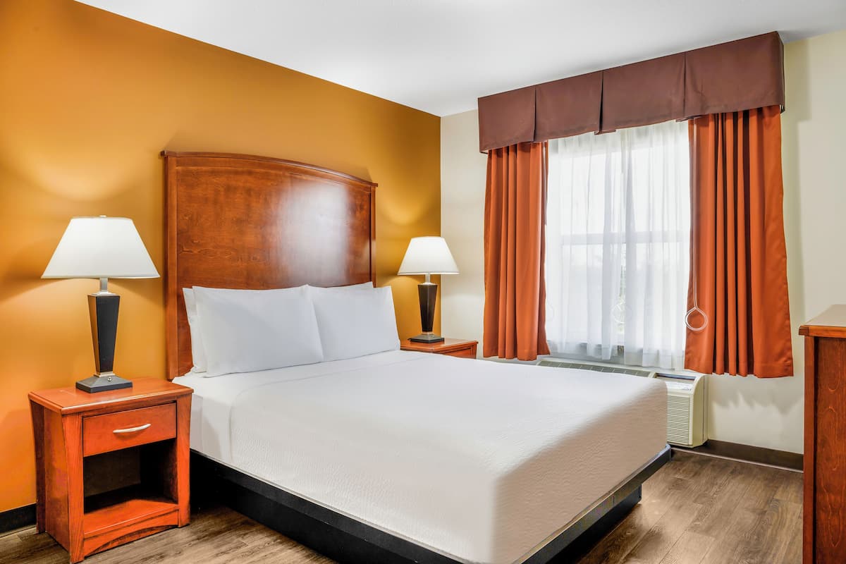 Habitación de hotel con una cama grande, dos mesitas de noche con lámparas, una ventana con cortinas y un cabecero de madera.