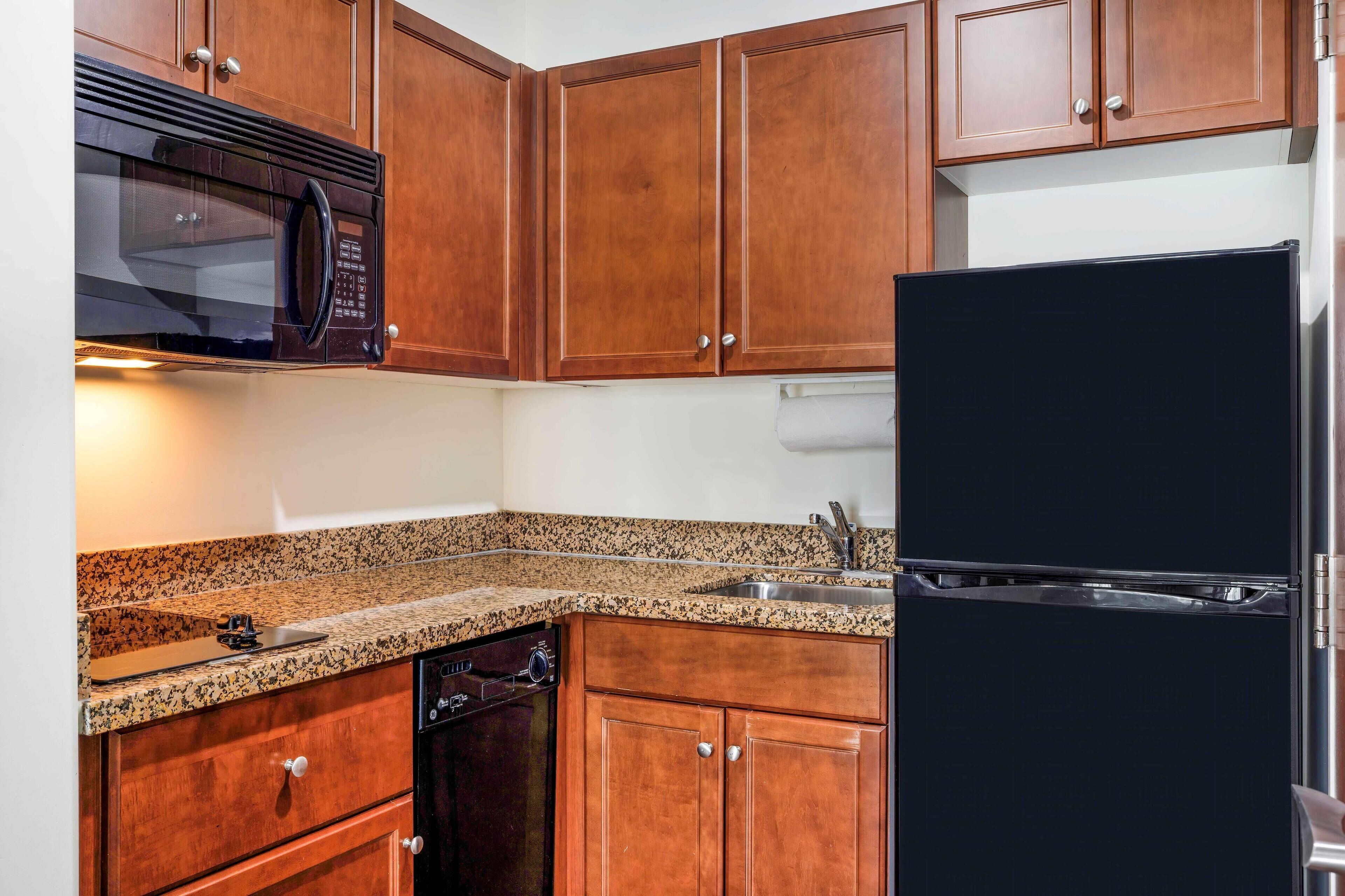 Una cocina con armarios de madera, microondas negro, refrigerador negro, encimera de granito y lavavajillas.