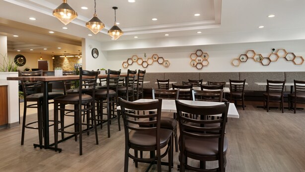 Un interior de restaurante moderno con varias mesas y sillas, iluminación colgante y decoraciones hexagonales en la pared.