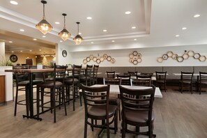 Un intérieur de restaurant moderne, avec de nombreuses tables et chaises, des luminaires suspendus et des décorations murales hexagonales.