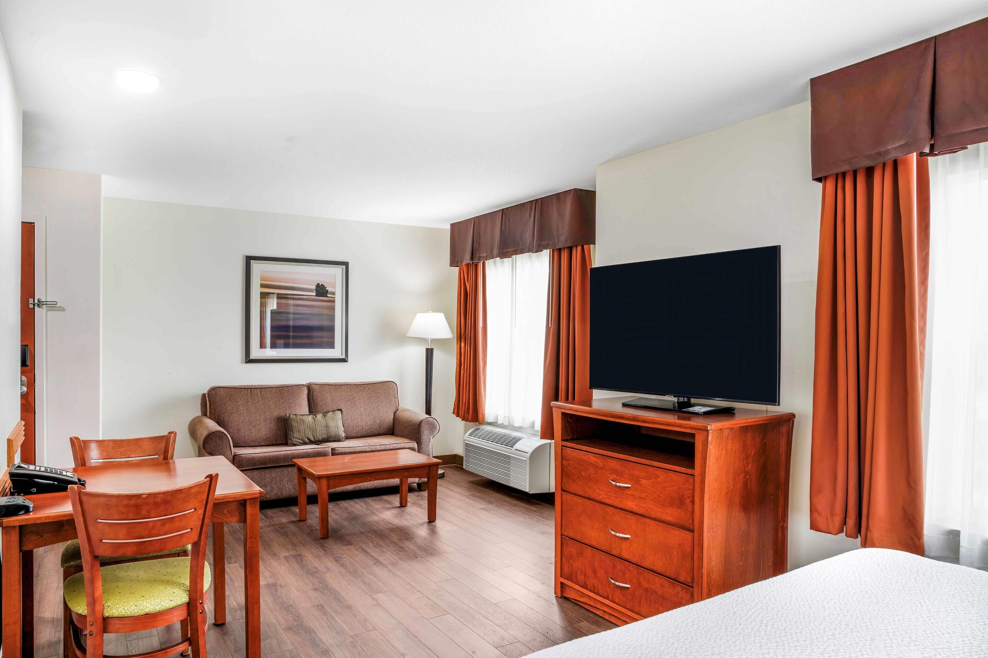A hotel room with a bed, a TV, a sofa, a coffee table, a desk with a chair, and a wardrobe.