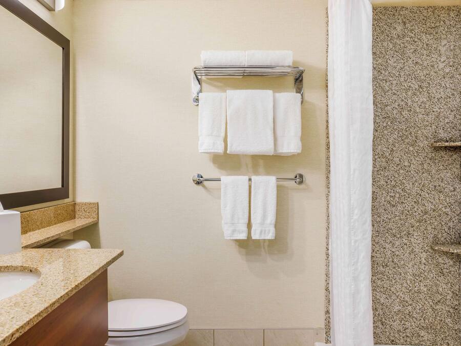 Een badkamer met toilet, wastafel en een handdoekrek met meerdere witte handdoeken.