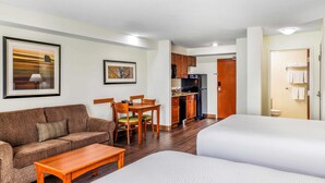 Habitación de hotel con sofá, mesa de comedor, sillas, zona de cocina con refrigerador y baño visible a través de una puerta abierta.