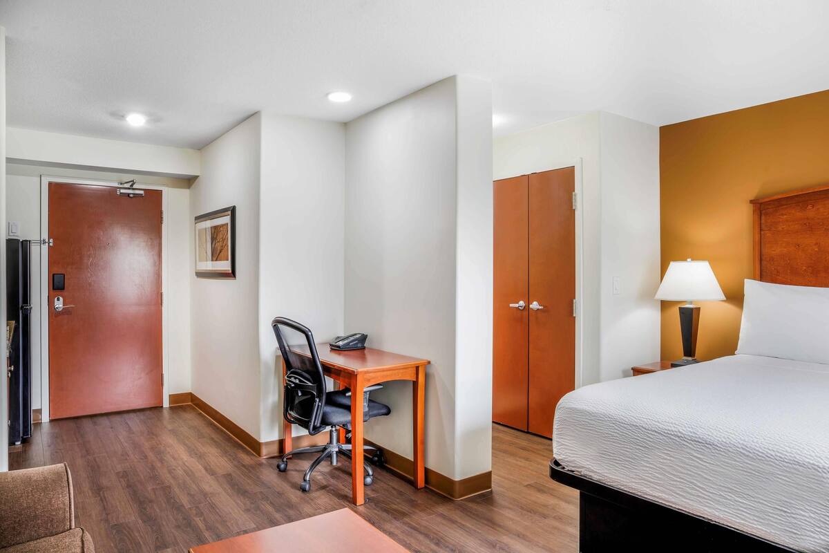 Una habitación de hotel con una cama, un escritorio con silla, un armario y una puerta.