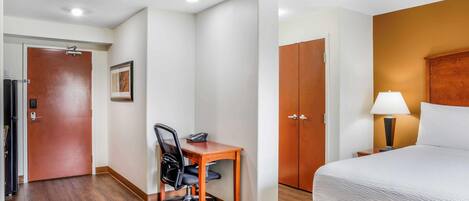 A hotel room with a bed, a desk with a chair, a wardrobe, and a door.