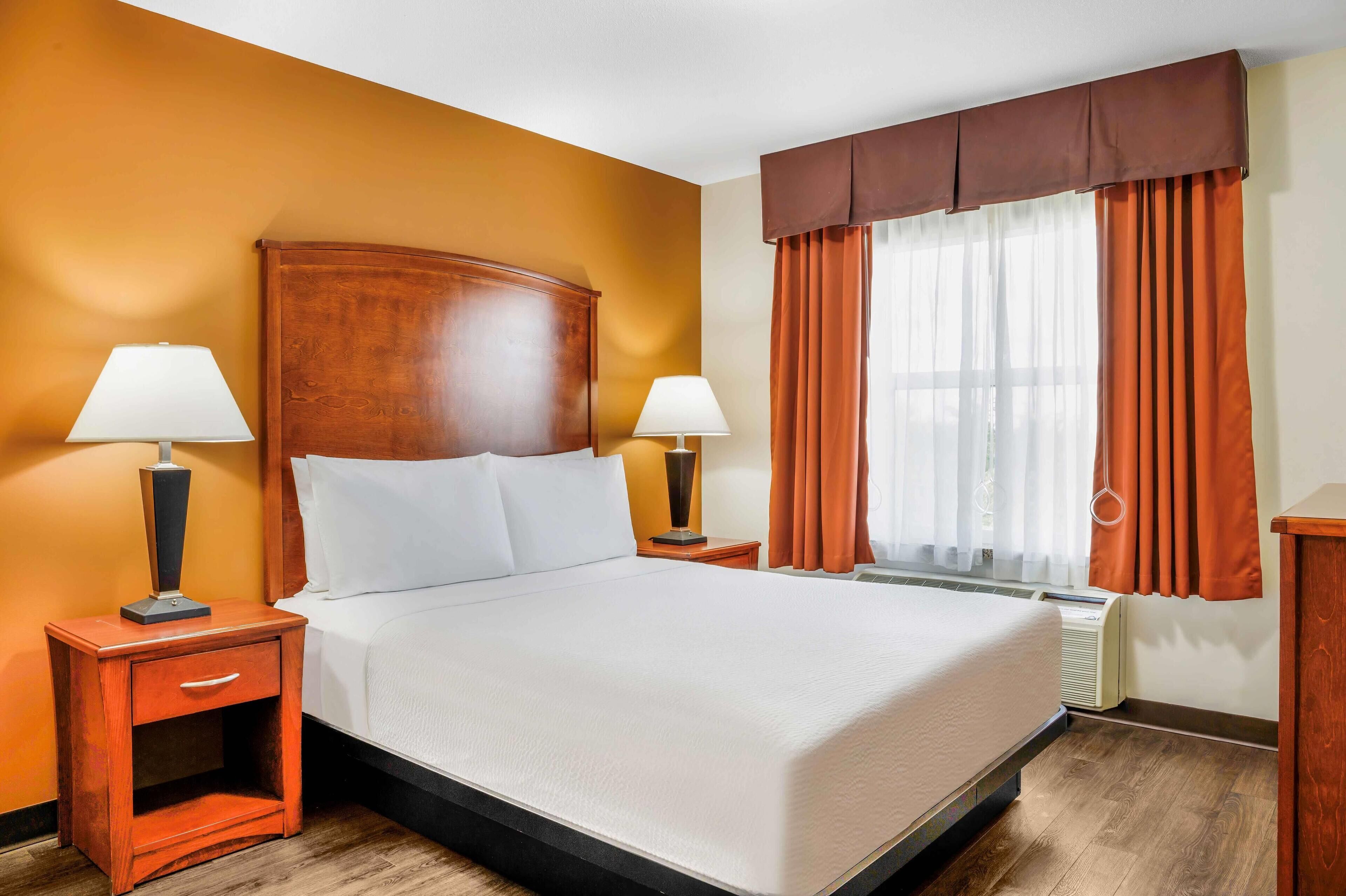 Camera d'albergo con un letto grande, due comodini con lampade, una finestra con tende e una testiera in legno.