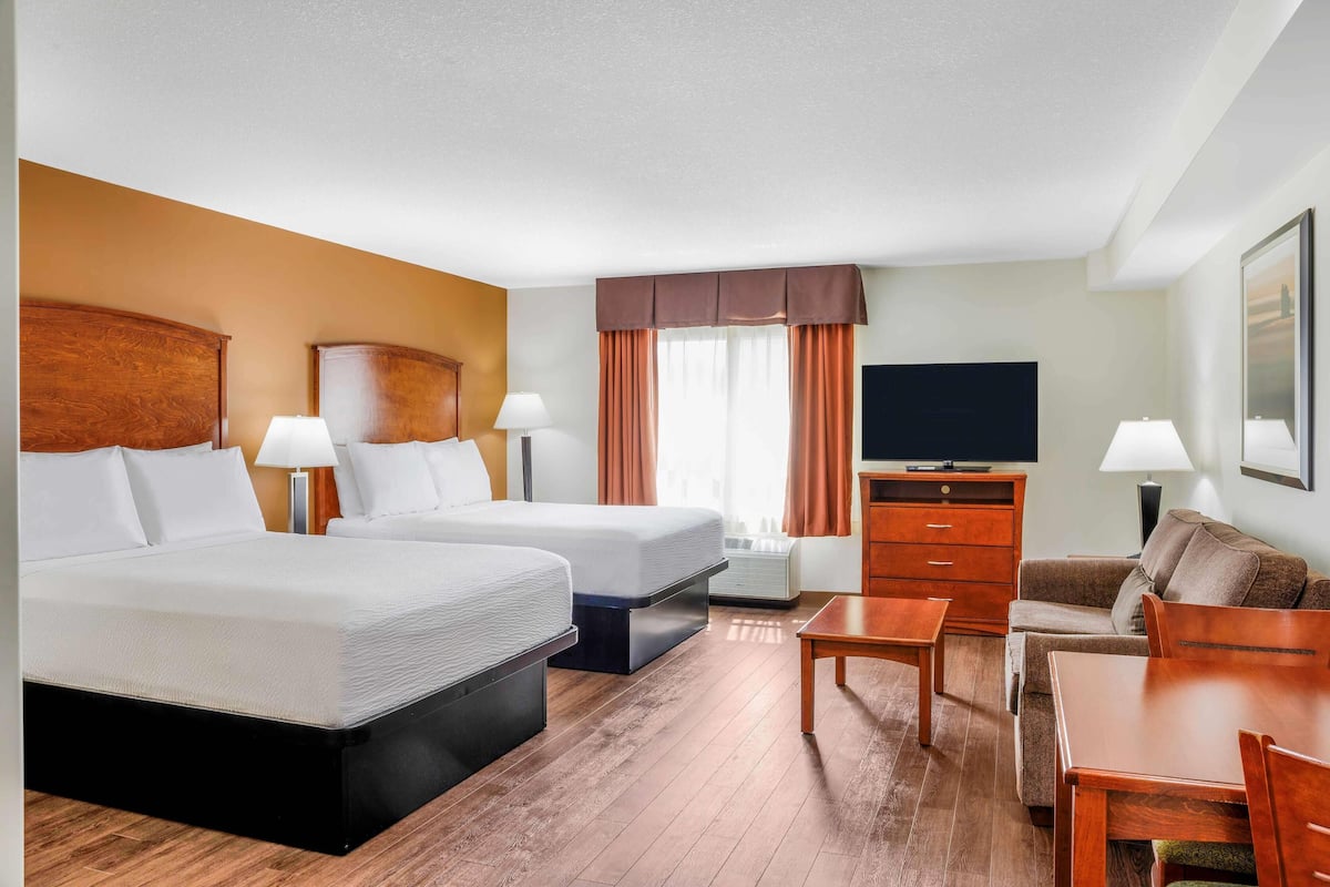 Una habitación de hotel con dos camas, televisión, sofá y mesa de comedor.
