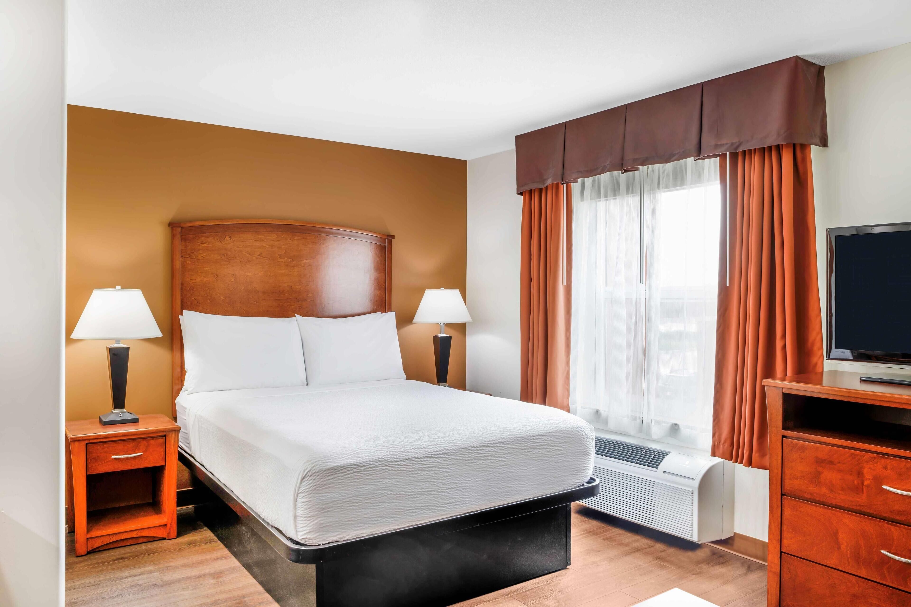 A hotel room with a large bed, two bedside tables with lamps, a TV, and a window with curtains.