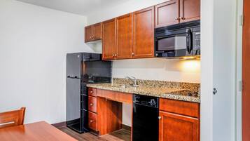 A compact kitchen with wooden cabinets, a black refrigerator, a microwave, and a dishwasher.